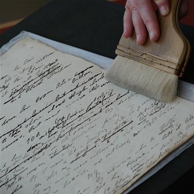 A handwritten manucript with a hand carefully brushing the page 