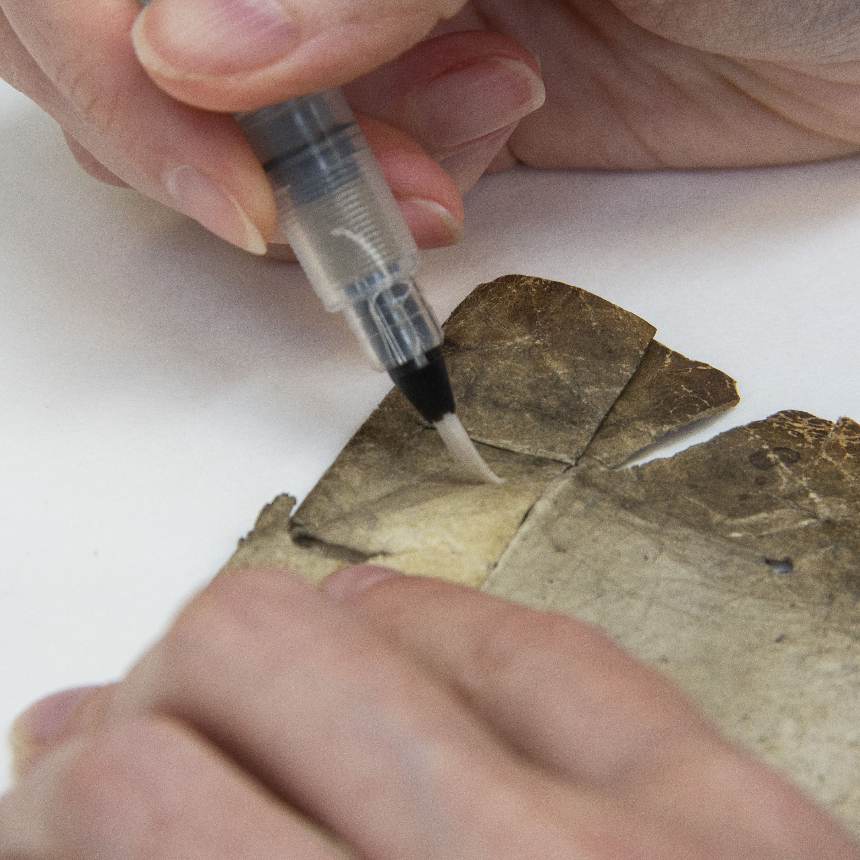 Two hands delicately glue parchment