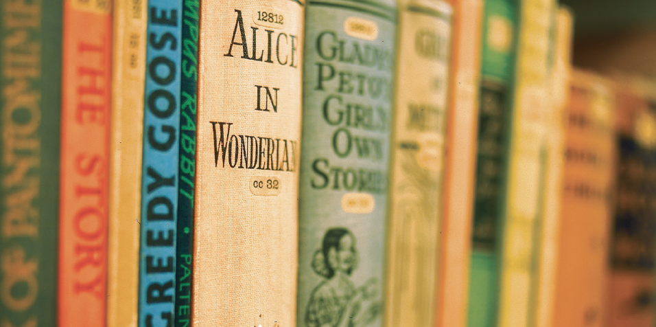 A group of hardback books on a shelf, with Alice and Wonderland in the foreground.