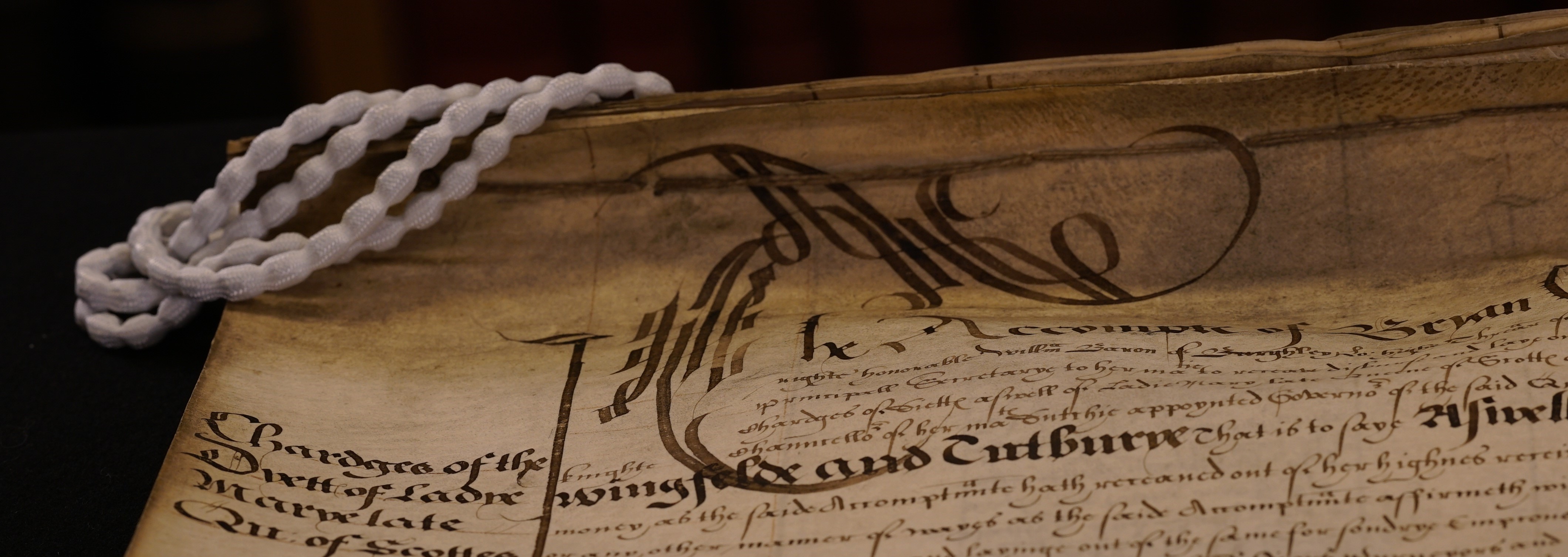 	A close up image of a beautiful manuscript with white weights that look like pearls on the top left hand corner.